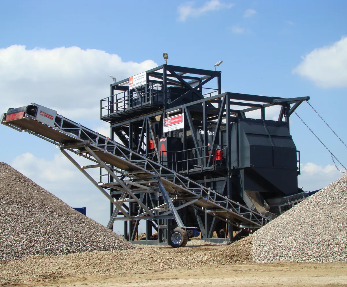 Zeefinstallatie met transportbanden en zand- en grinddepots onder een blauwe lucht